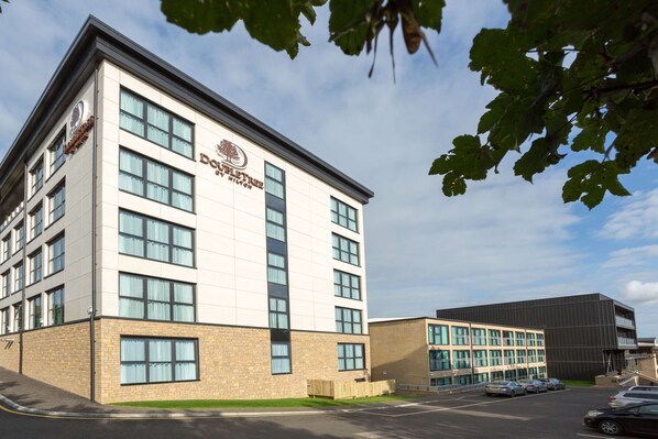 A modern building with a sign reading "Dover Hotel." It features multiple floors, large windows, and a parking lot with several cars.