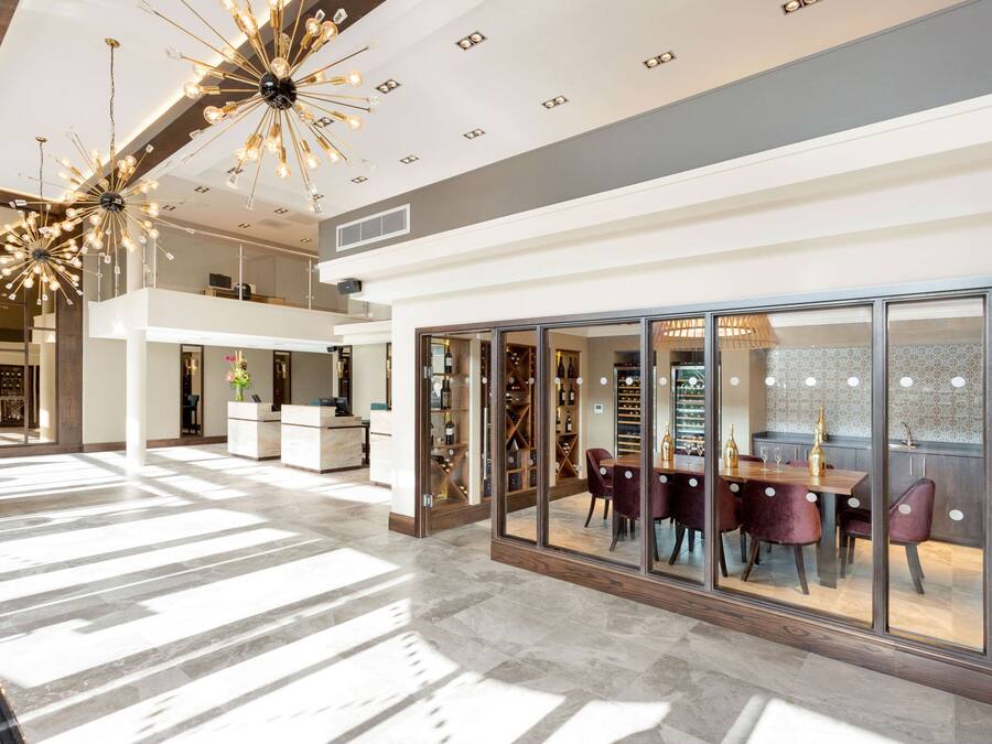 A spacious, well-lit interior with a high ceiling, modern chandeliers, and a dining area with a view through large glass doors.