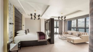 A modern hotel room with a large bed, a sofa, a TV, and a view of the city. - DoubleTree by Hilton Edinburgh - Queensferry Crossing (Dunfermline)