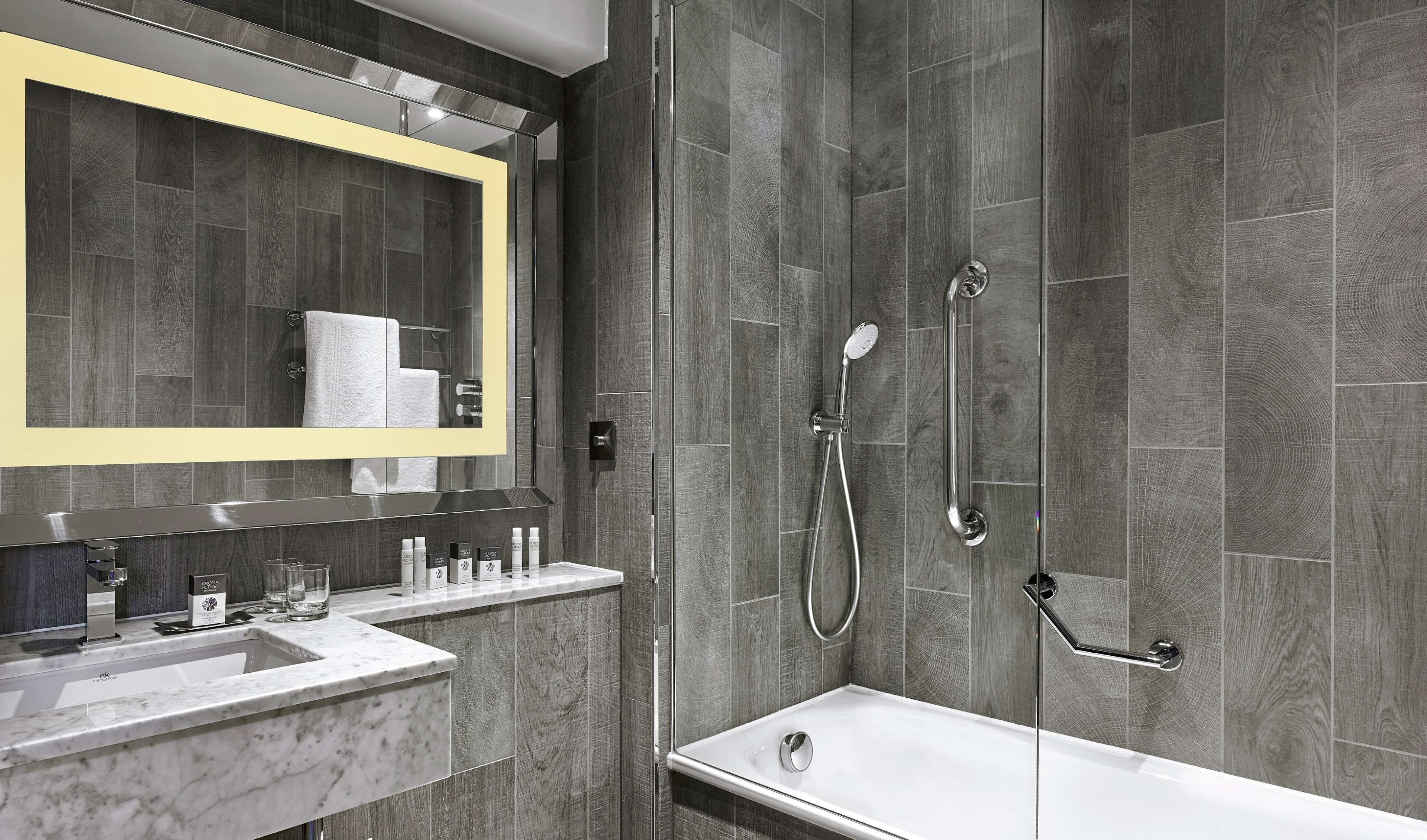 A modern bathroom with a large mirror, two sinks, a bathtub, and a shower with a handheld showerhead.