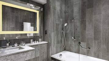 A modern bathroom with a large mirror, two sinks, a bathtub, and a shower with a handheld showerhead.