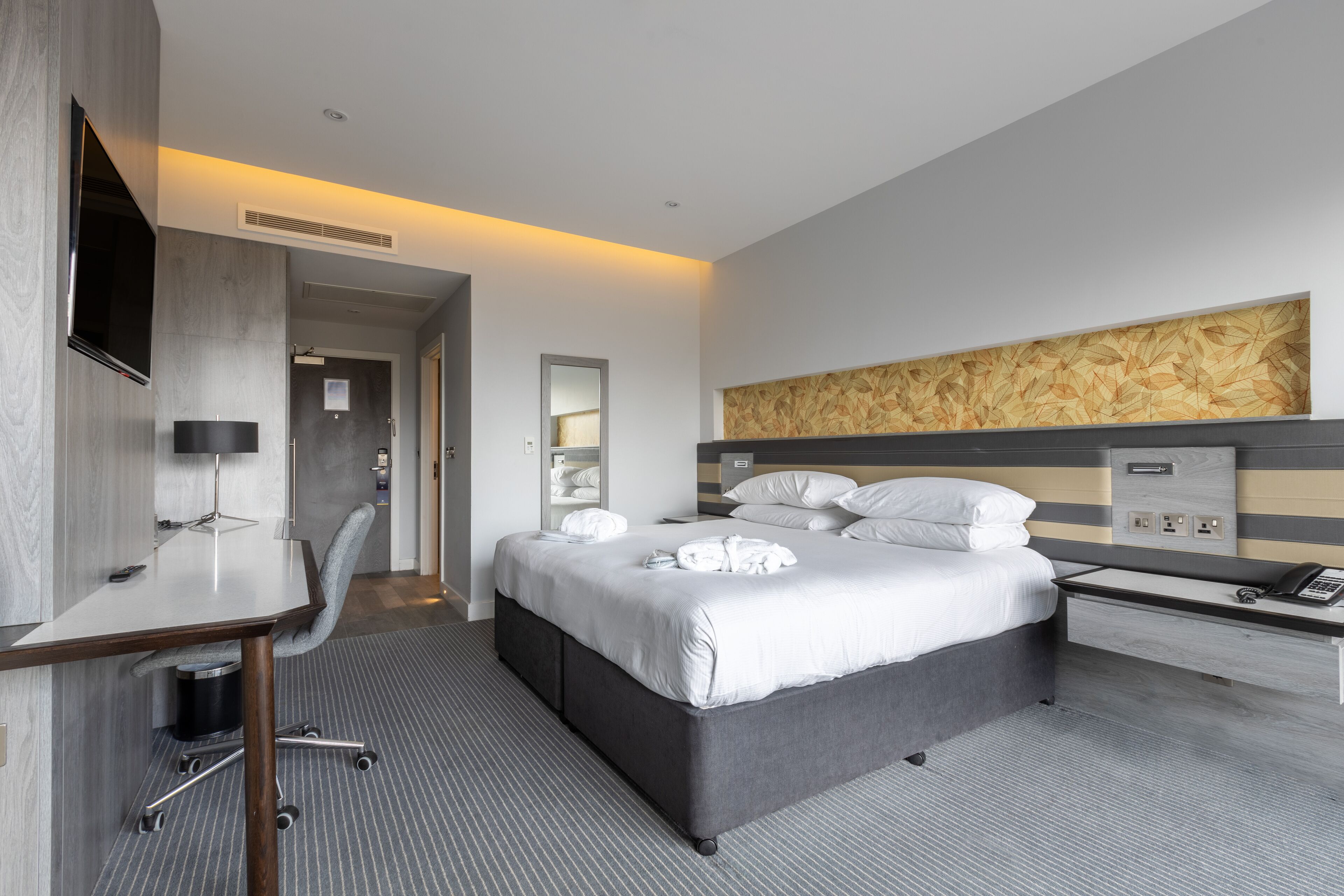 Ein modernes Hotelzimmer mit Bett, Schreibtisch, Stuhl und einem großen Spiegel.
