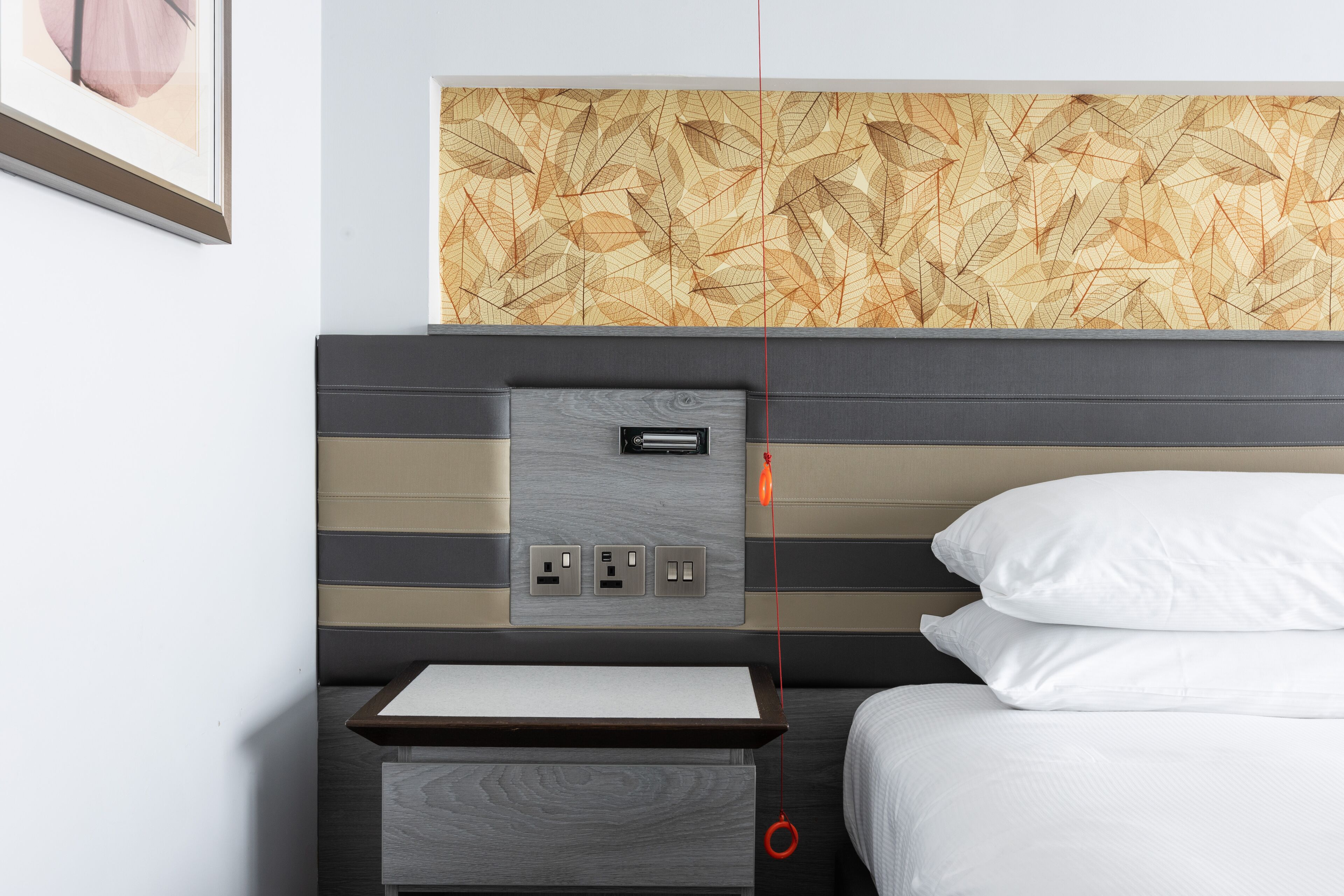 Una habitación de hotel moderna con cabecera de madera, una mesita de noche y un enchufe.