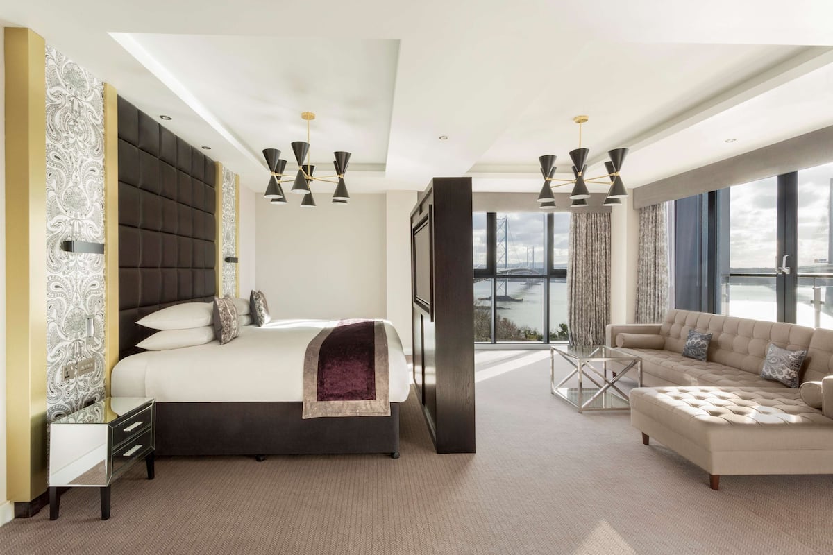 A modern bedroom with a large bed, a sofa, and a view of the city.