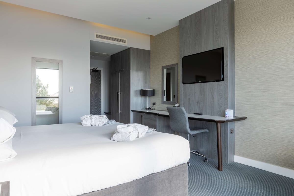 A modern hotel room with a large bed, a desk, a chair, and a flat-screen TV mounted on the wall.