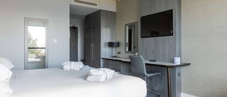 A modern hotel room with a large bed, a desk, a chair, and a flat-screen TV mounted on the wall.