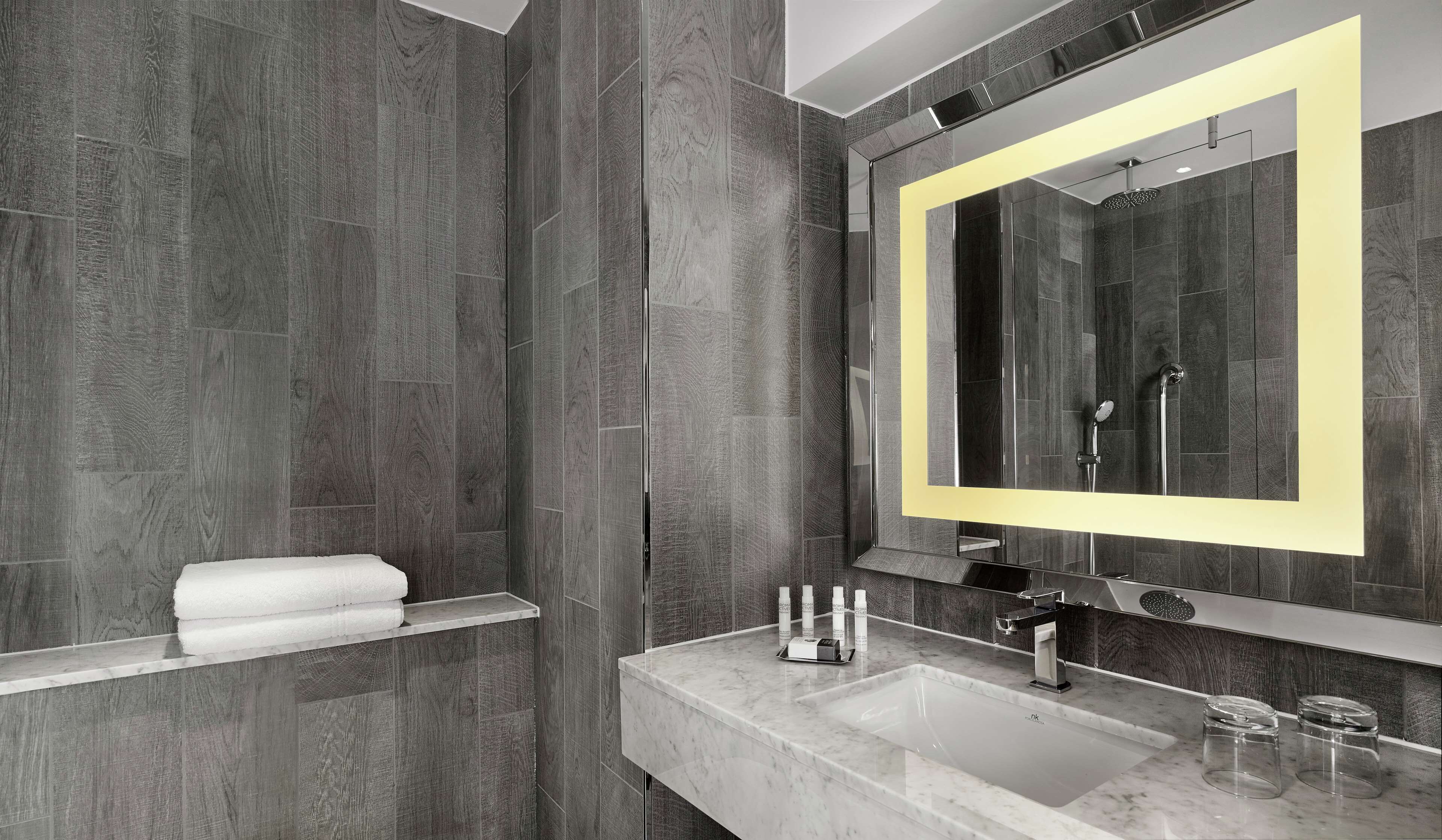 A modern bathroom with a large mirror, a marble sink, and a towel rack.