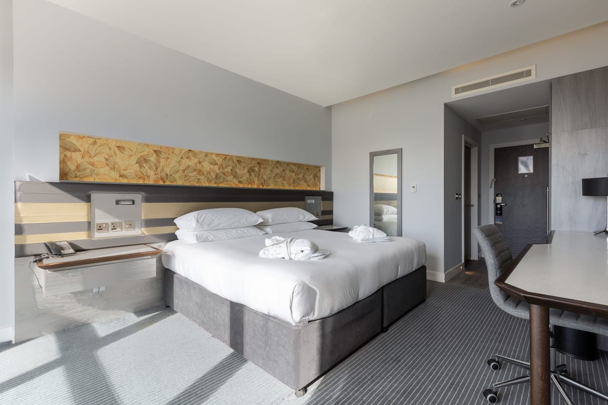 A modern hotel room with a large bed, bedside tables, a desk, and a shower area.