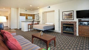 A hotel room with a sofa, a small table, a bed, a kitchenette, a fireplace, and a television. - WorldMark Clear Lake (Nice)
