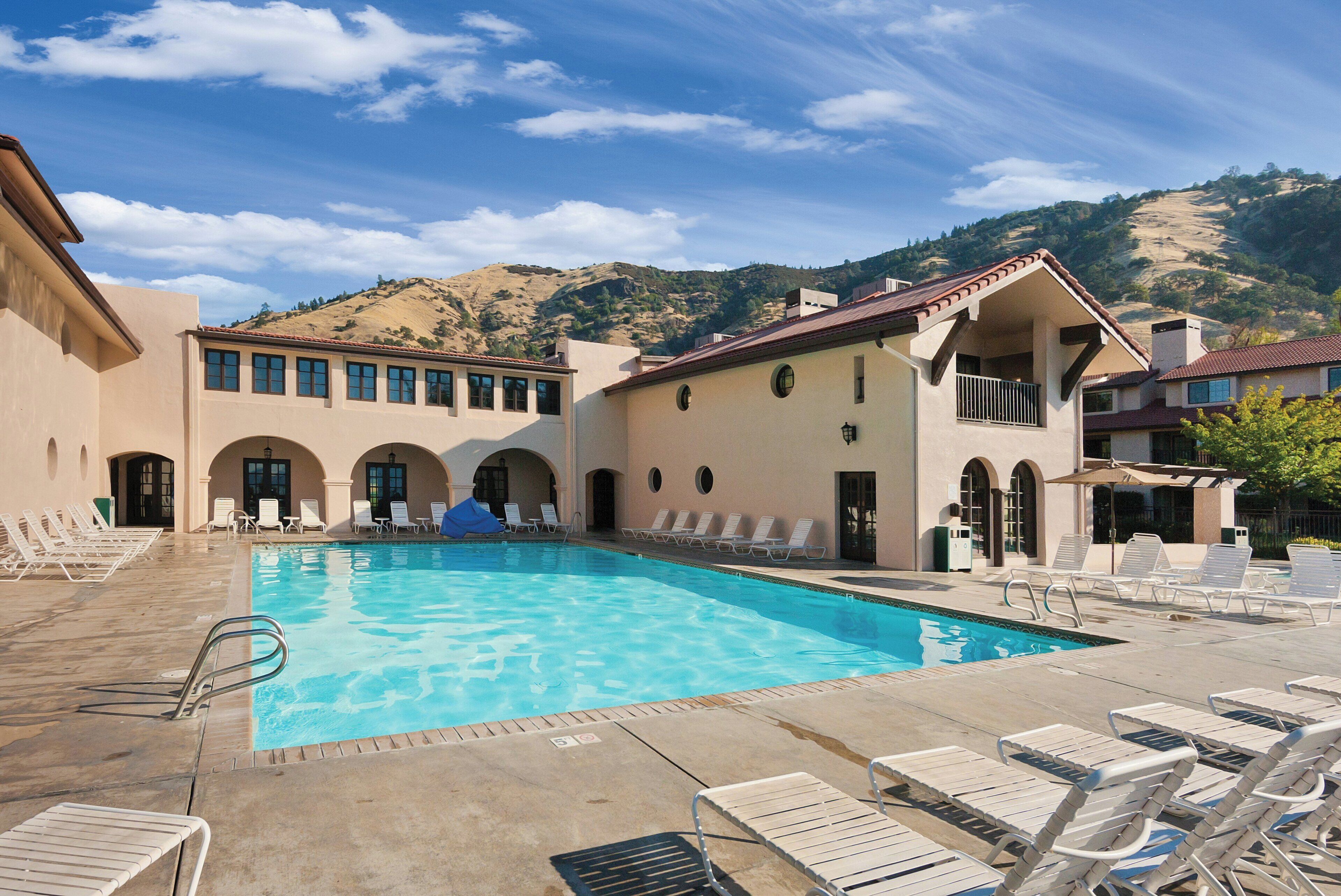 A swimming pool with lounge chairs, a covered area, and a mountainous backdrop.