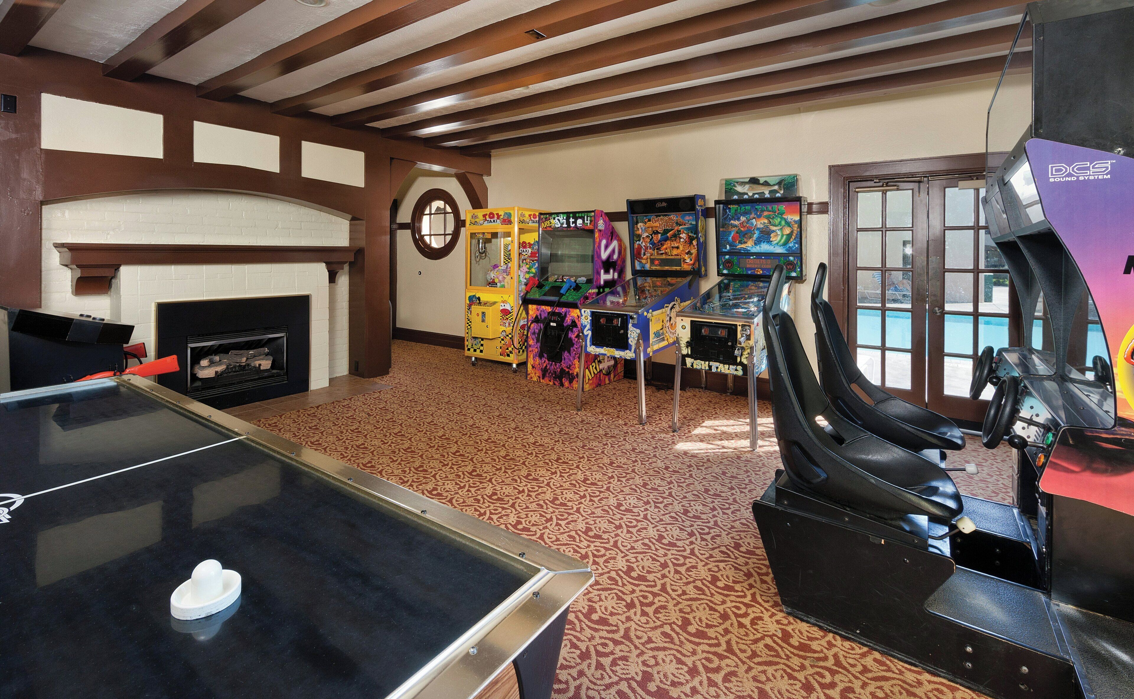 Una habitación con mesa de ping pong, juegos de arcade, dardos y chimenea.
