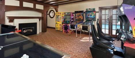 Una habitación con mesa de ping pong, juegos de arcade, dardos y chimenea.