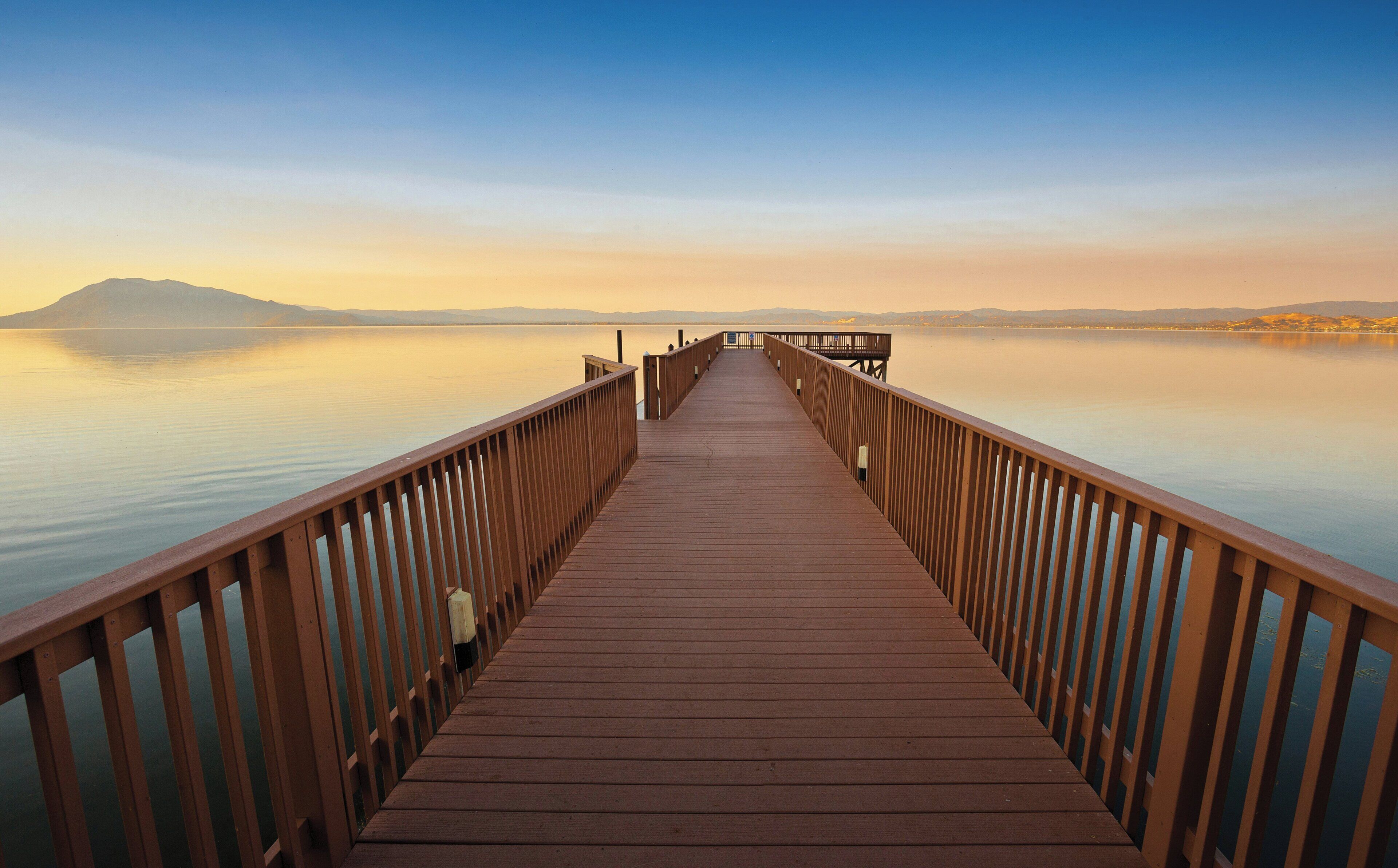 A wooden pier extending into calm water with a clear sky above.