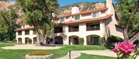 A two-story building with a red-tiled roof, multiple balconies, and a well-maintained lawn with flower beds.