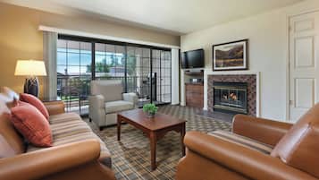 A living room with leather sofas, a patterned armchair, a television, a fireplace, and a view through large windows.