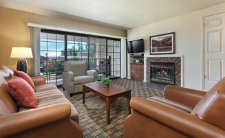 Una sala de estar con sofás de cuero, un sillón estampado, un televisor, una chimenea y vistas amplias por grandes ventanales.