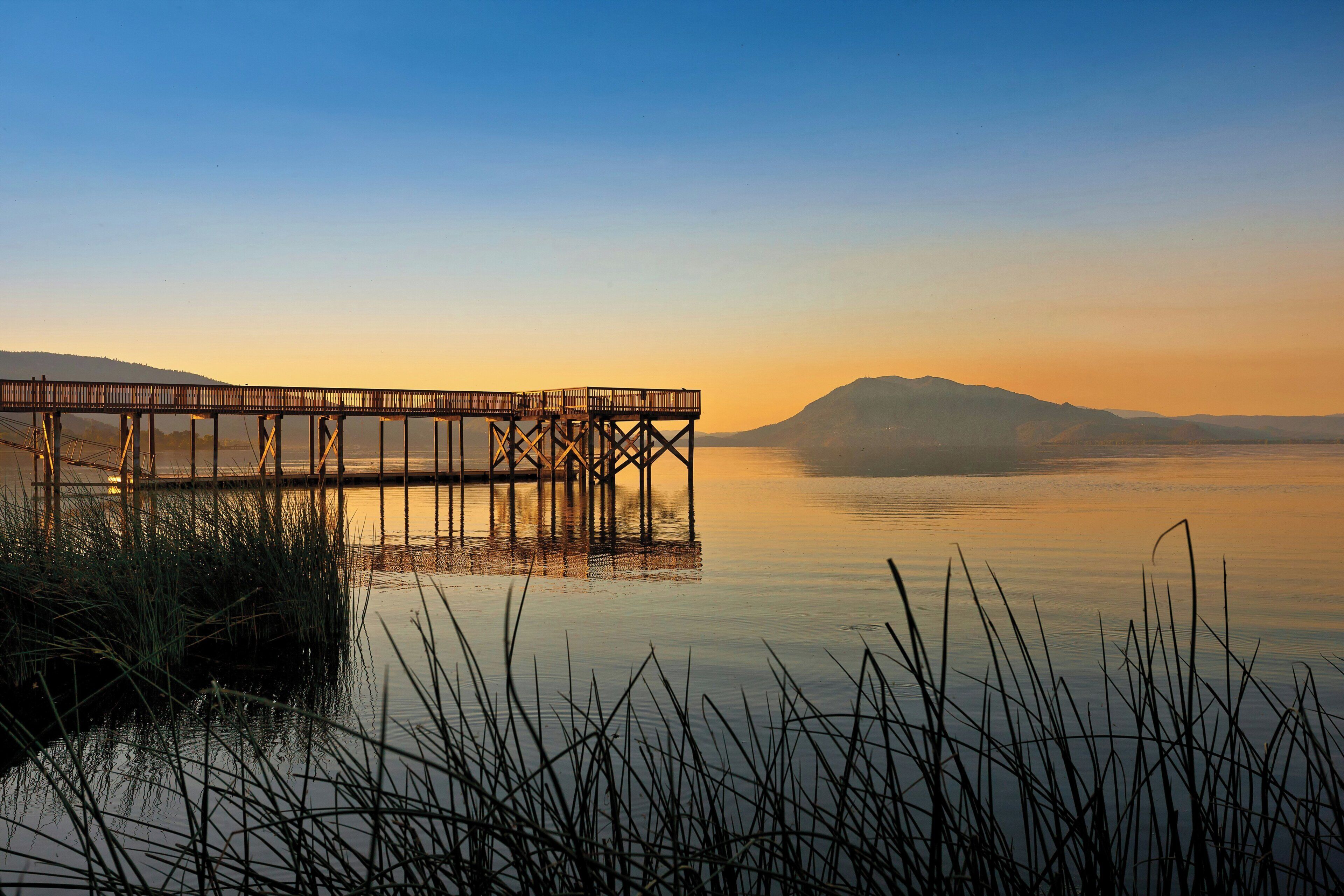 A pier extending into calm water with a mountain in the background.