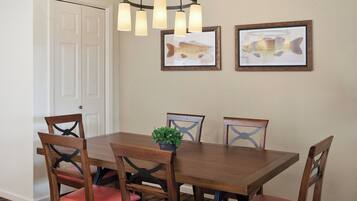 A dining area with a wooden table, six chairs, a potted plant, and two framed fish illustrations on the wall.