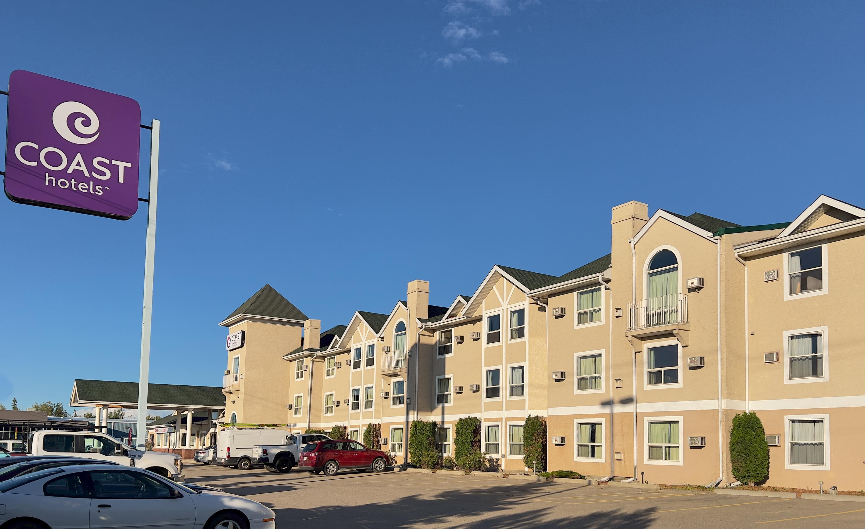 Edifício de hotel com vários andares, estacionamento e placa da Coast Hotels.