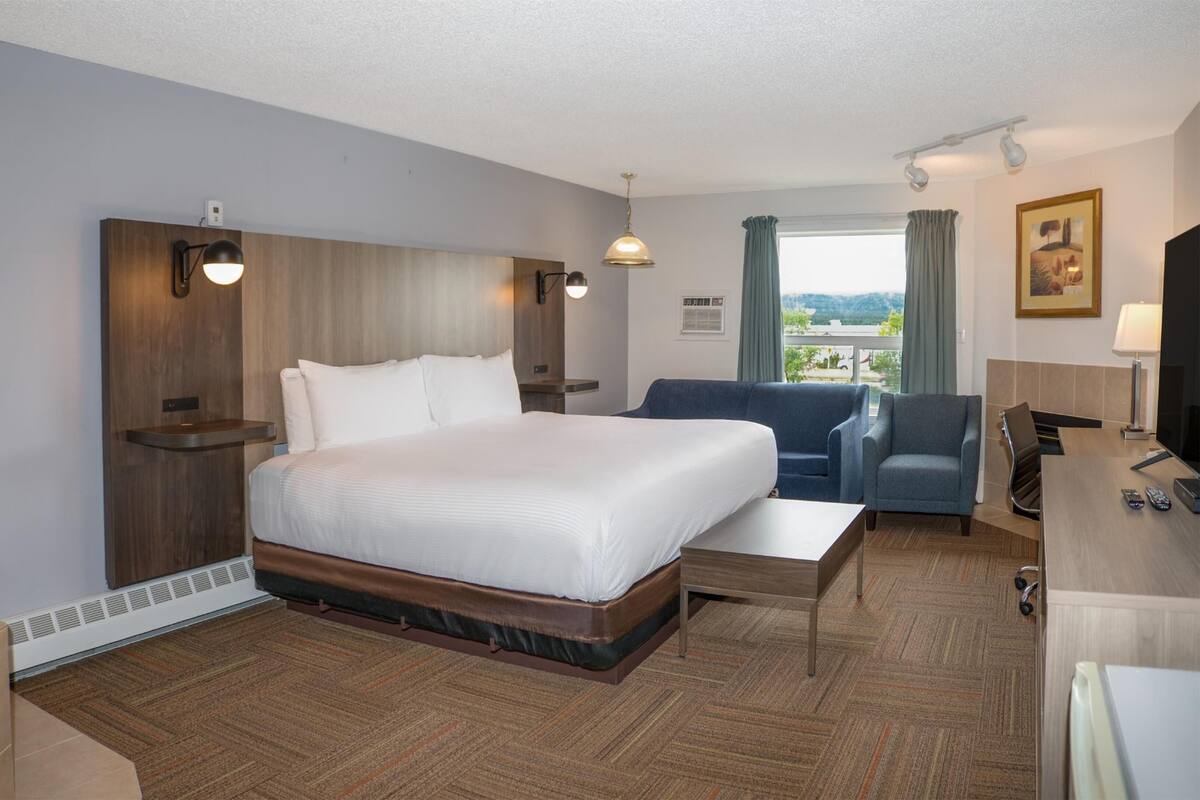 A hotel room with a large bed, a sofa, a desk with a TV, and a view of the outdoors.