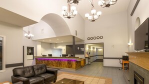 A modern lobby with leather sofas, a glass-top coffee table, a reception desk, and a fireplace. - Coast Hinton Hotel (Hinton)