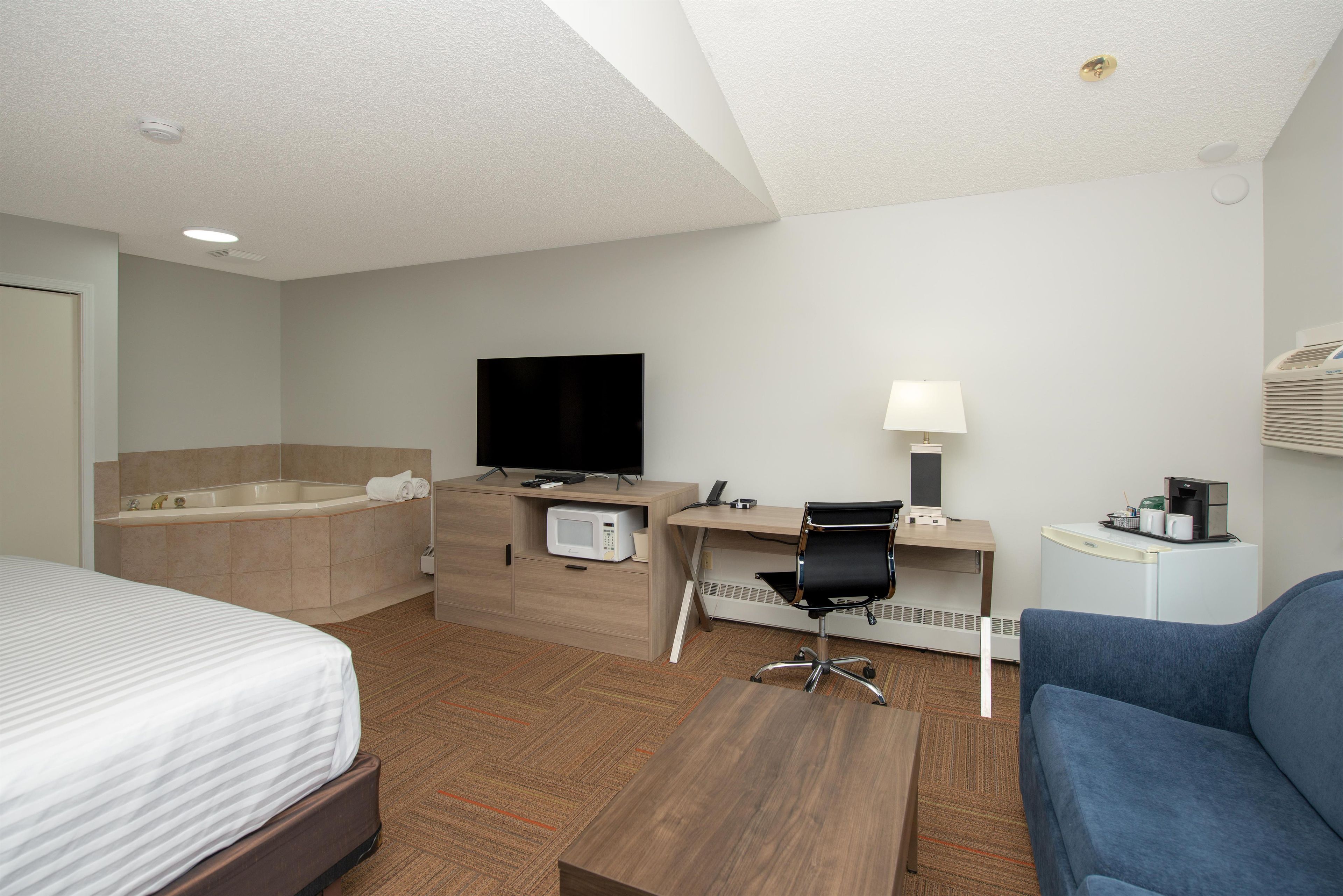 A hotel room with a bed, a desk, a chair, a television, a coffee machine, and a bathroom with a bathtub.