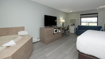 Quarto de hotel com cama, escrivaninha com computador, televisão, banheiro com banheira e janela com vista.