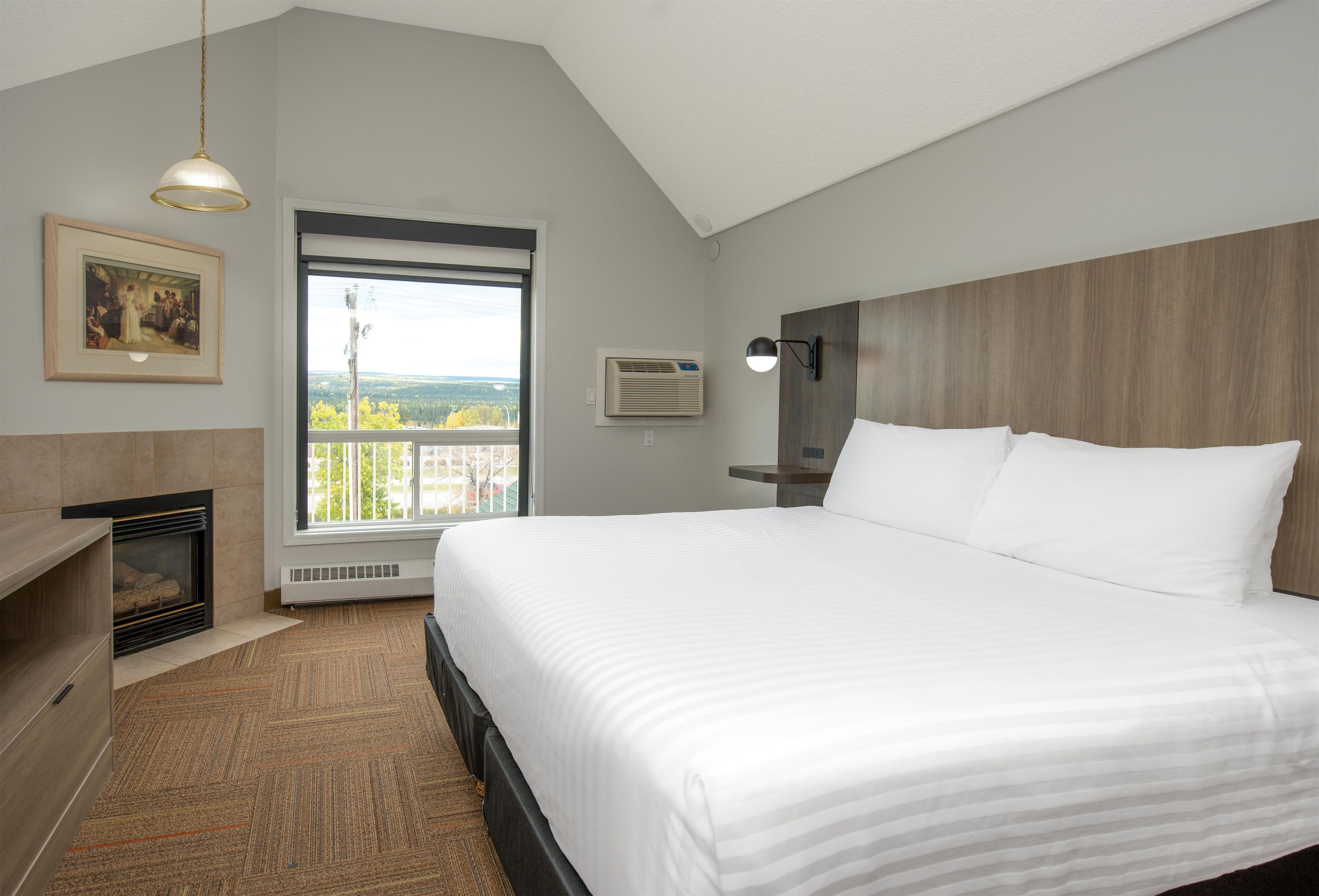 Quarto de hotel com uma cama grande, lareira, janela com vista e um quadro na parede.