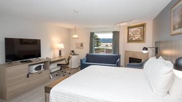 A hotel room with a bed, desk, chair, TV, and a fireplace.