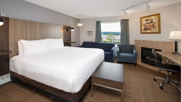 A hotel room with a large bed, a desk with a chair, a sofa, and a fireplace. - Coast Hinton Hotel (Hinton)