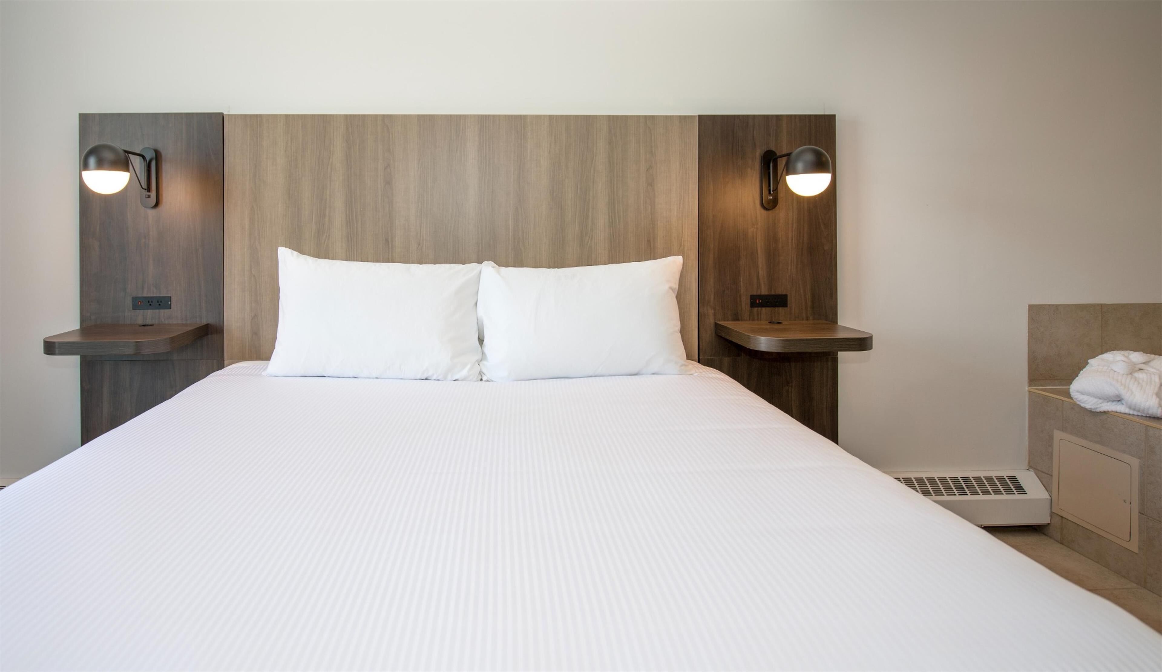 A hotel room with a large bed, two bedside tables with lamps, a headboard, and a small heater.