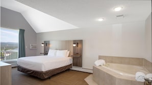 A modern hotel room with a large bed, a separate bathroom with a bathtub, and a view of the outdoors. - Coast Hinton Hotel (Hinton)