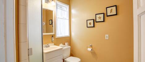 A bathroom with a toilet, sink, and mirror. There are three framed pictures on the wall.