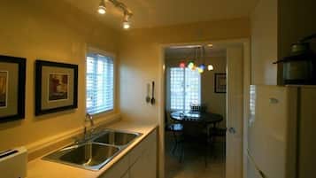 A compact kitchen with a double sink, a dining area with a table and chairs, and a refrigerator.