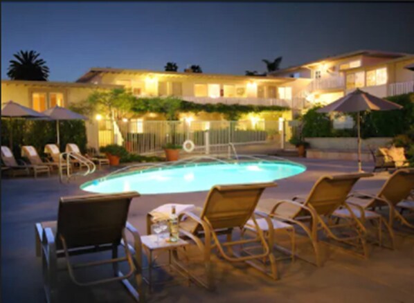 A pool area with lounge chairs and umbrellas, surrounded by a building with multiple windows and a railing. - The Tides Laguna Beach (Laguna Beach)