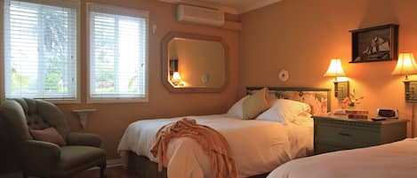 A bedroom with two beds, a chair, a nightstand with lamps, and a large mirror.