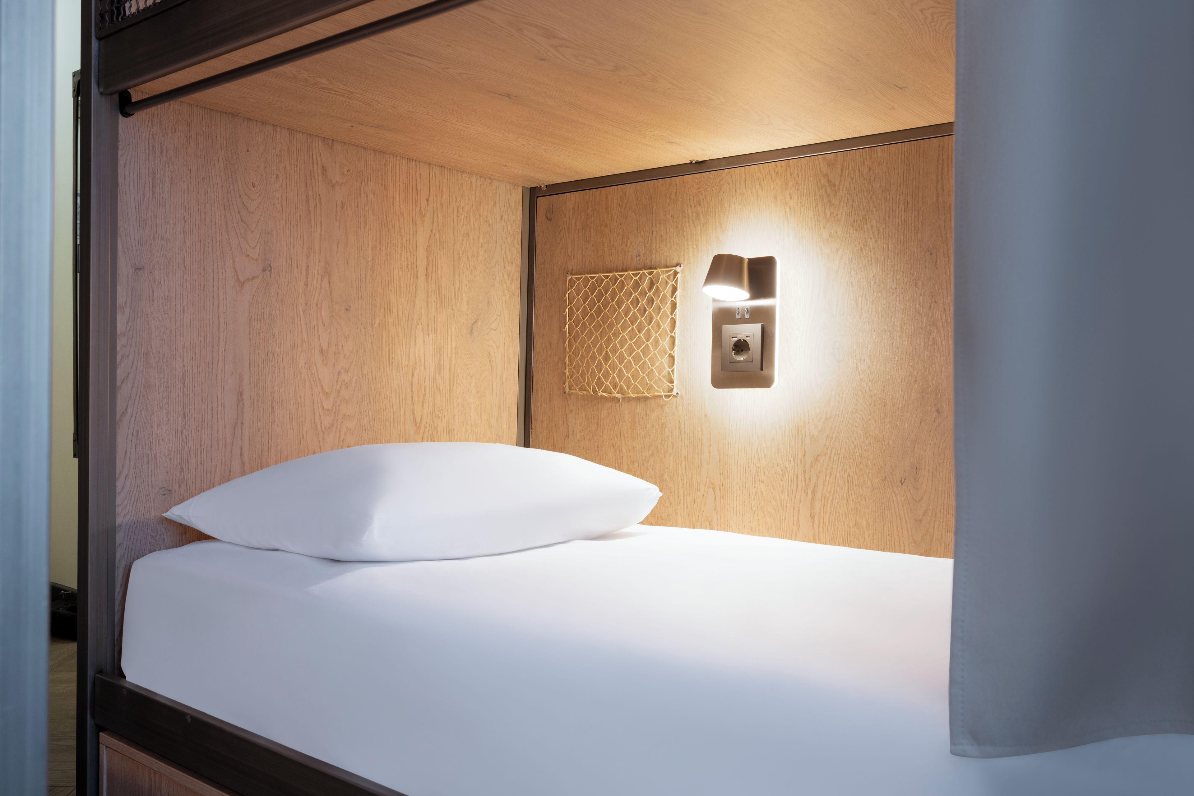 Una cama individual con almohada blanca y cabecera, un aplique de pared y un enchufe.