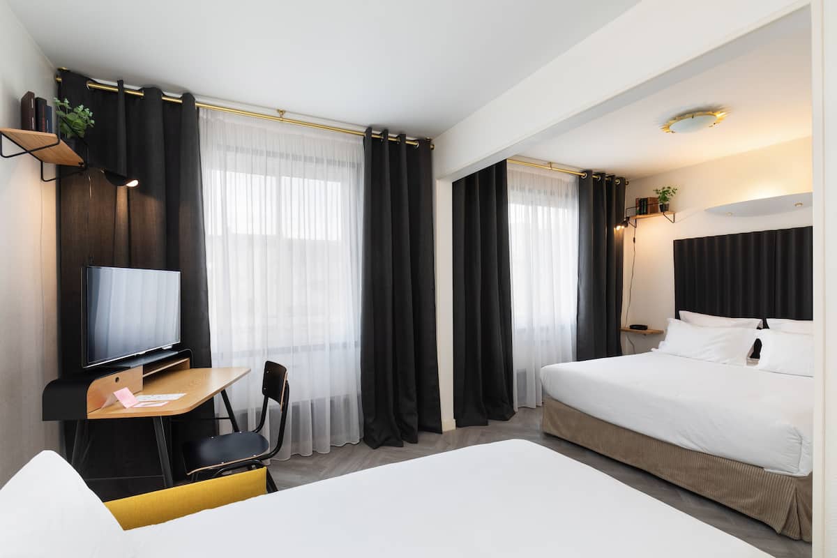 Una habitación de hotel moderna con cama, escritorio con silla, televisión y un amplio ventanal con cortinas.