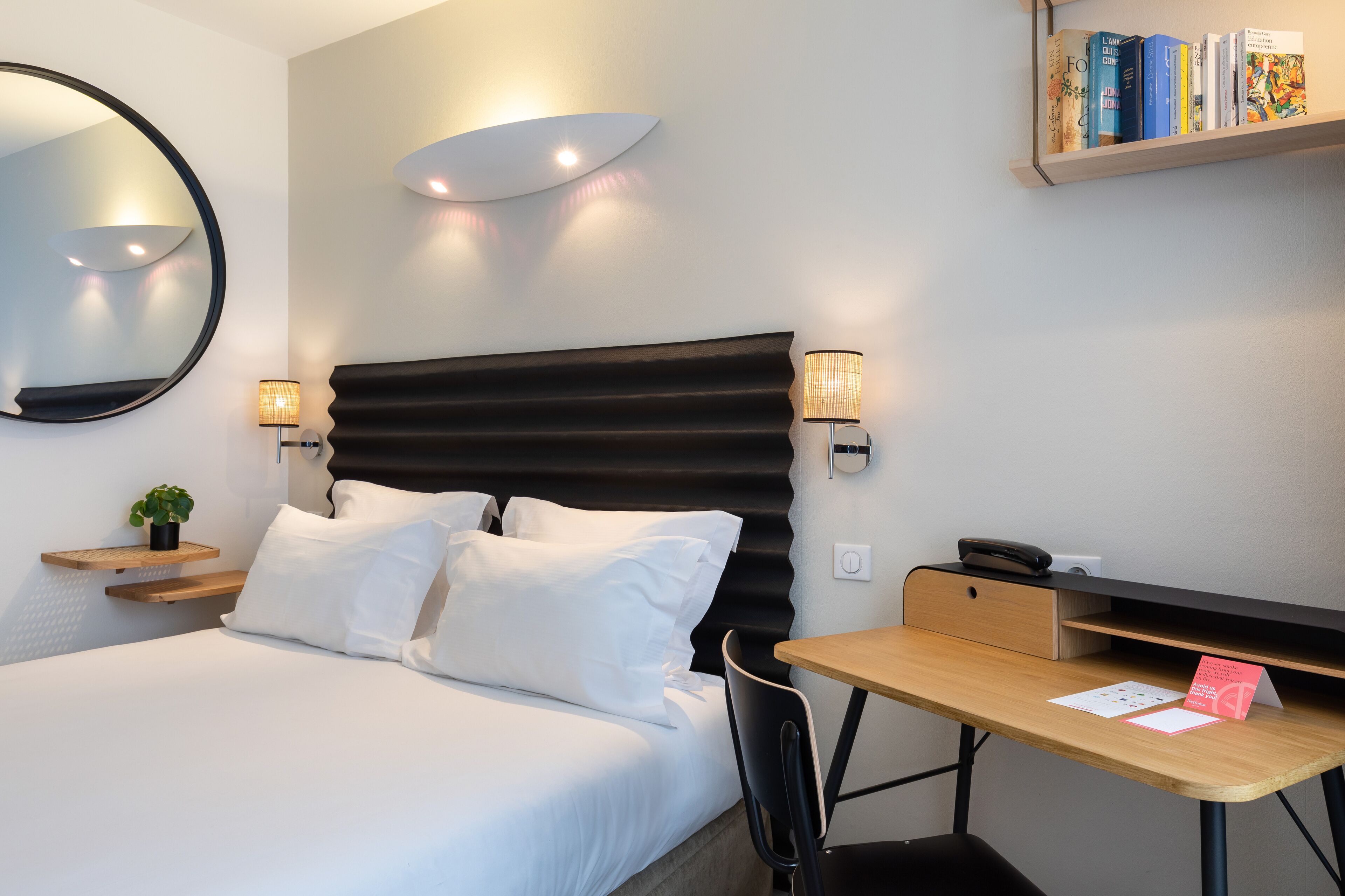 Una habitación de hotel moderna con una cama grande, lámparas de noche, un escritorio y una estantería.