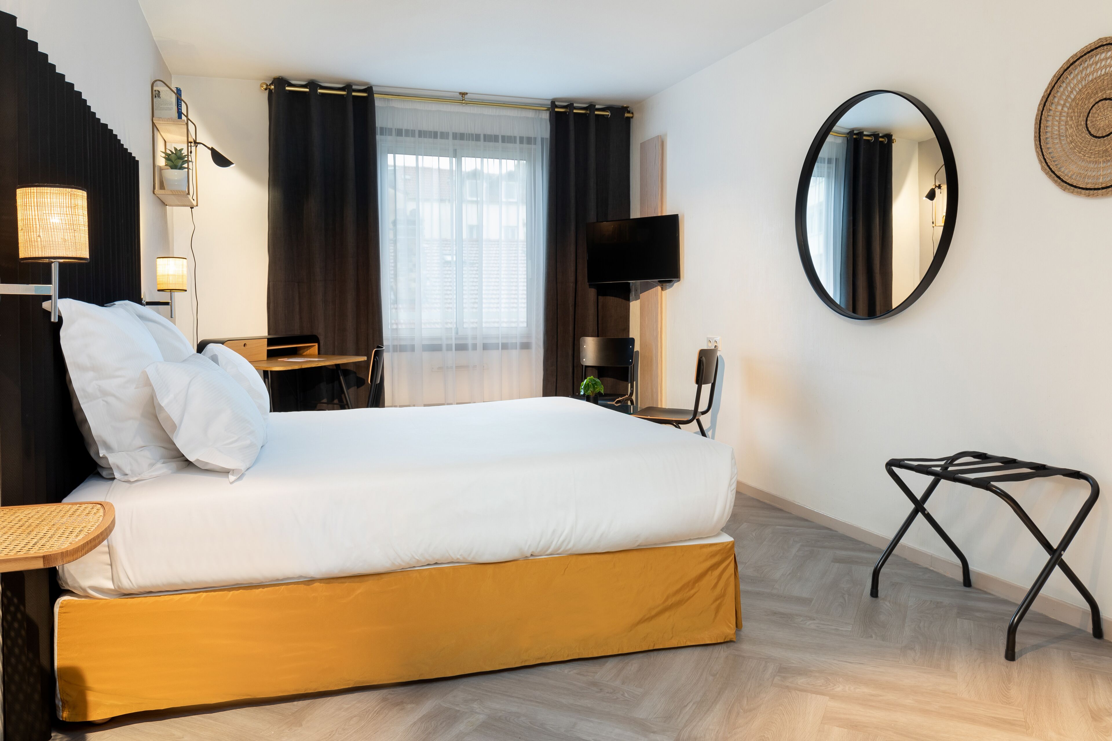 Une chambre d’hôtel équipée d’un lit, d’un bureau, d’une chaise, d’une télévision, d’un miroir et d’une fenêtre avec des rideaux.