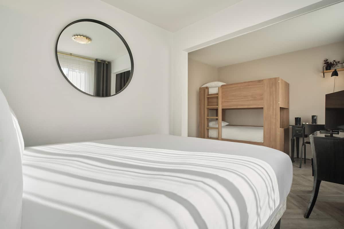 Una habitación de hotel moderna con una cama grande, una cama nido de madera, un escritorio y un televisor.