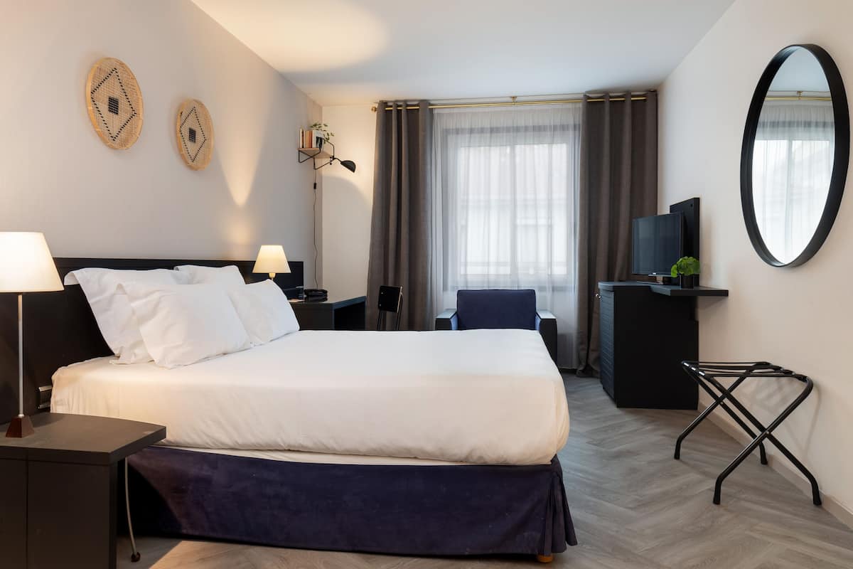 Habitación de hotel con una cama grande, mesitas de noche, un escritorio con silla, un televisor y un espejo.