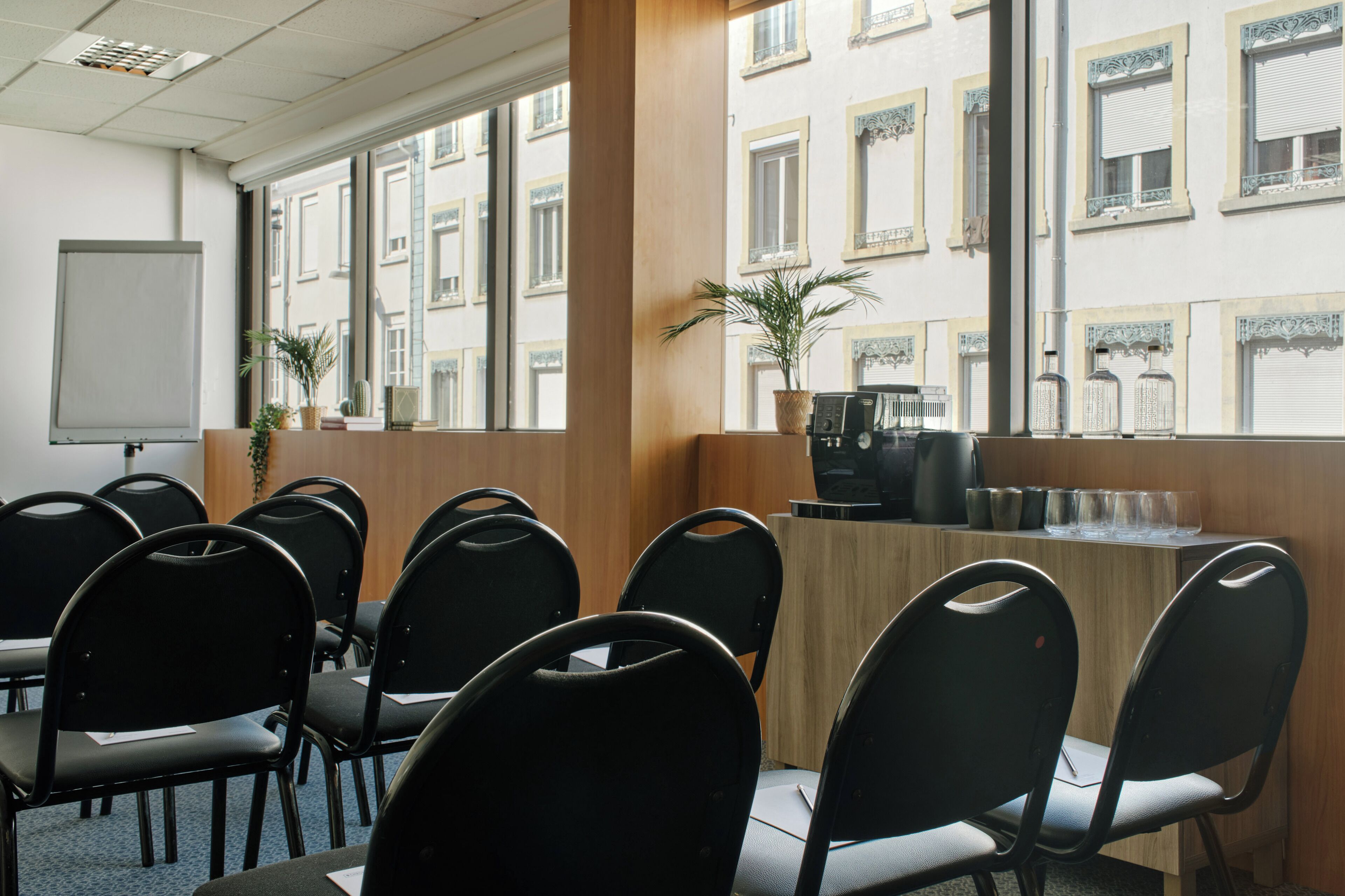 Una sala de conferències amb cadires negres, una taula de fusta, una pissarra i una finestra amb vista a un edifici.