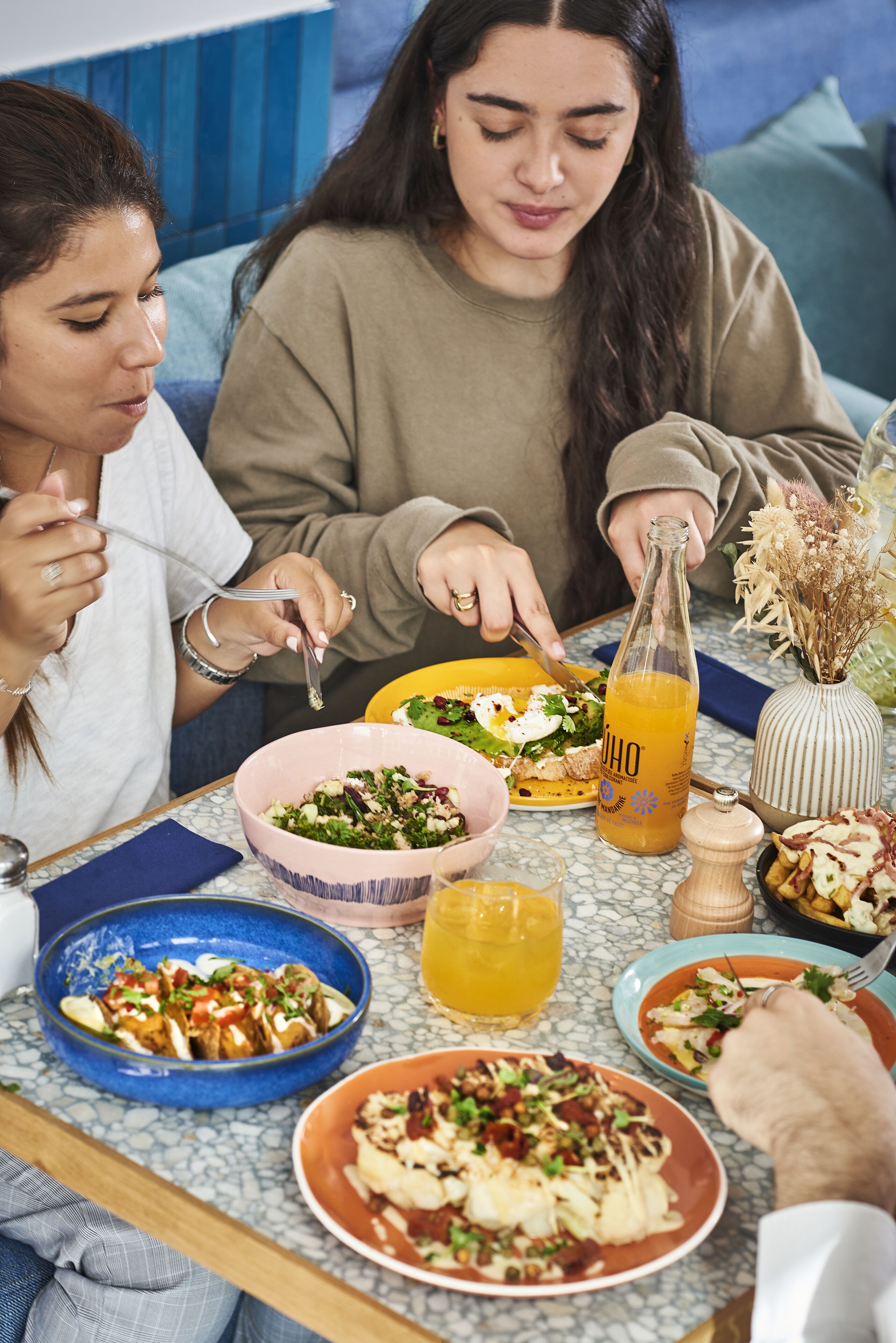 Una mesa de comedor con varios platos, una botella de jugo y un florero con flores secas.
