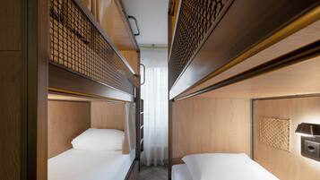 A narrow train compartment with two single beds, wooden paneling, and a small overhead shelf.