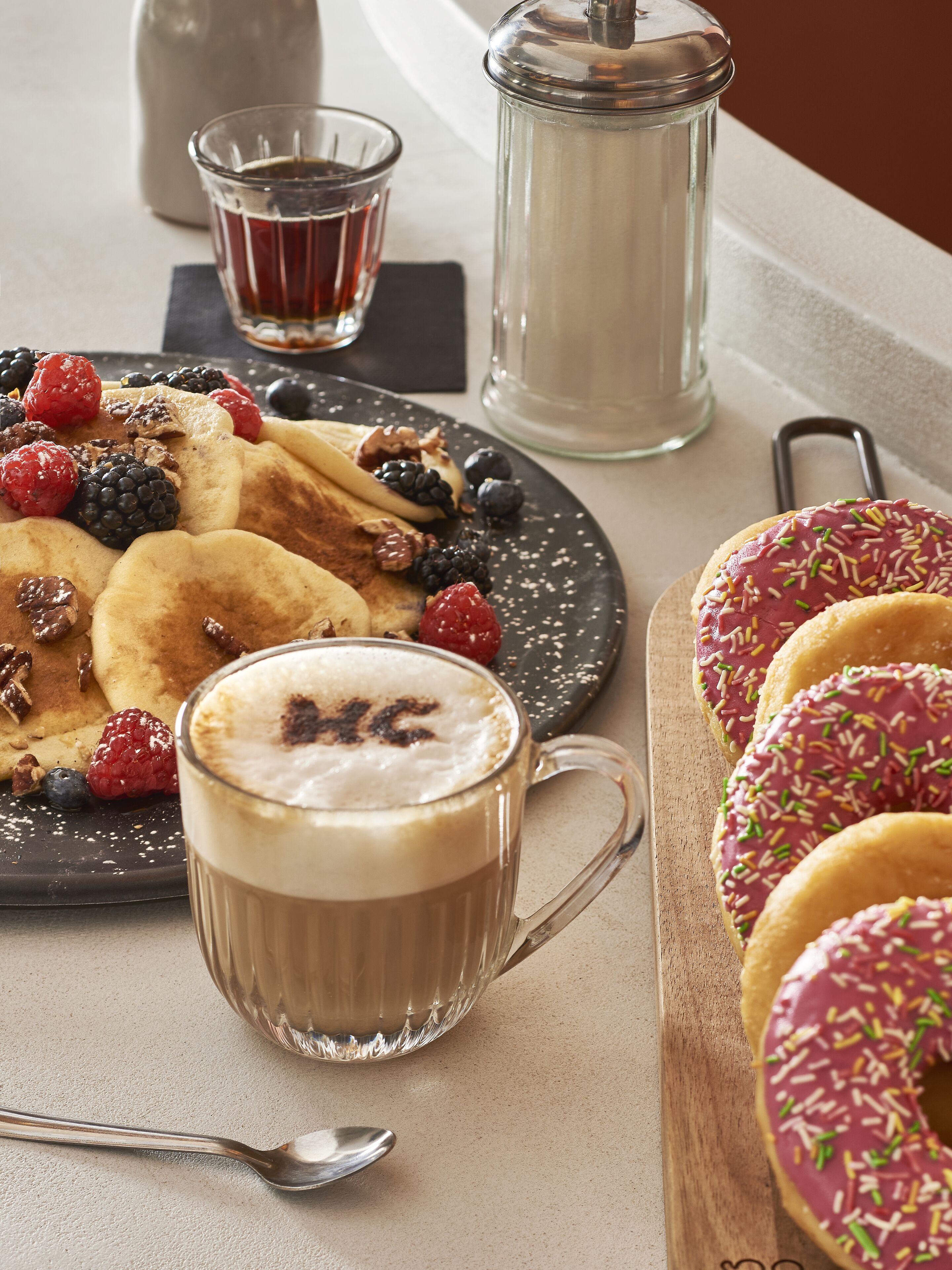 Un desayuno con tortitas, bayas, una taza de café y rosquillas.