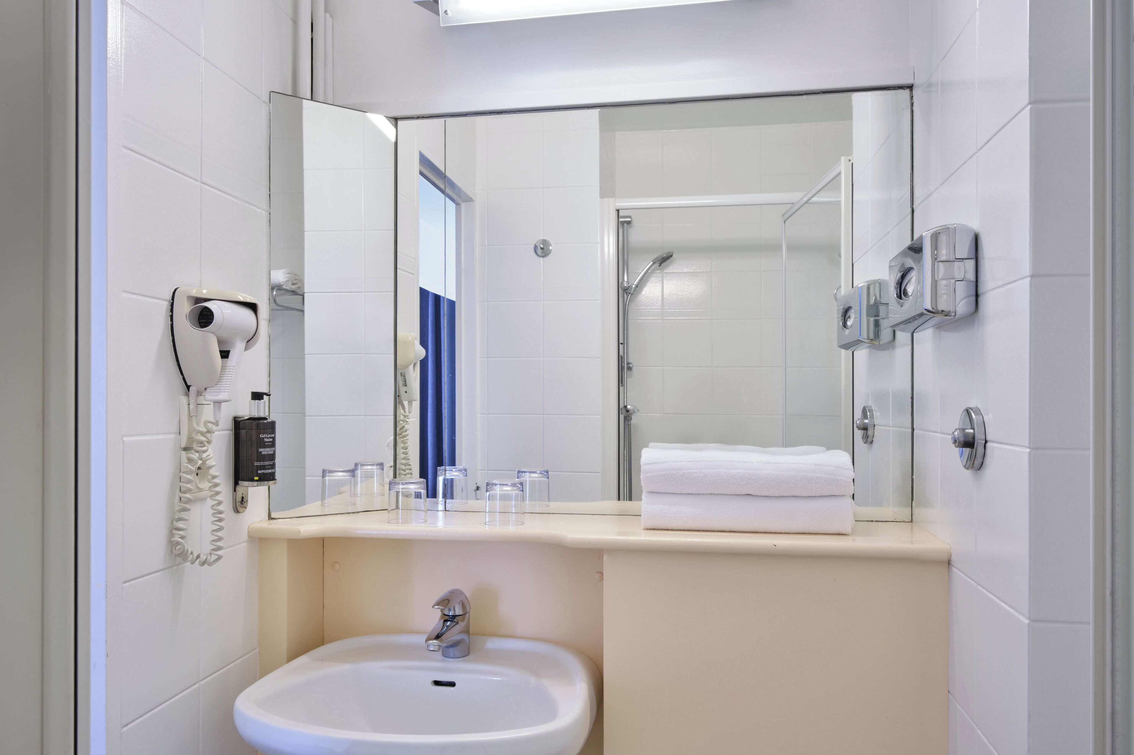 A bathroom with a sink, mirror, towel rack, and a hairdryer on the wall.