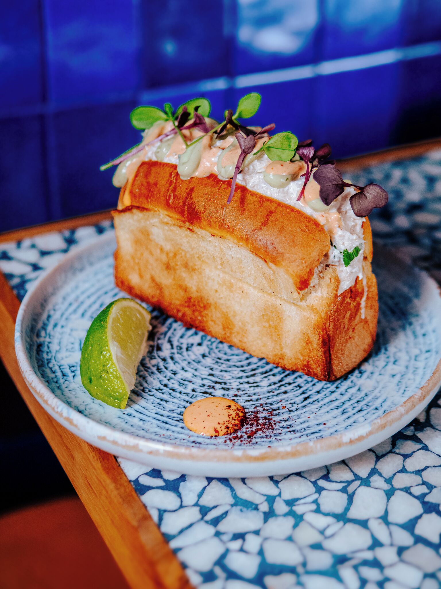 A sandwich on a ceramic plate with a lime wedge and a small red pepper.