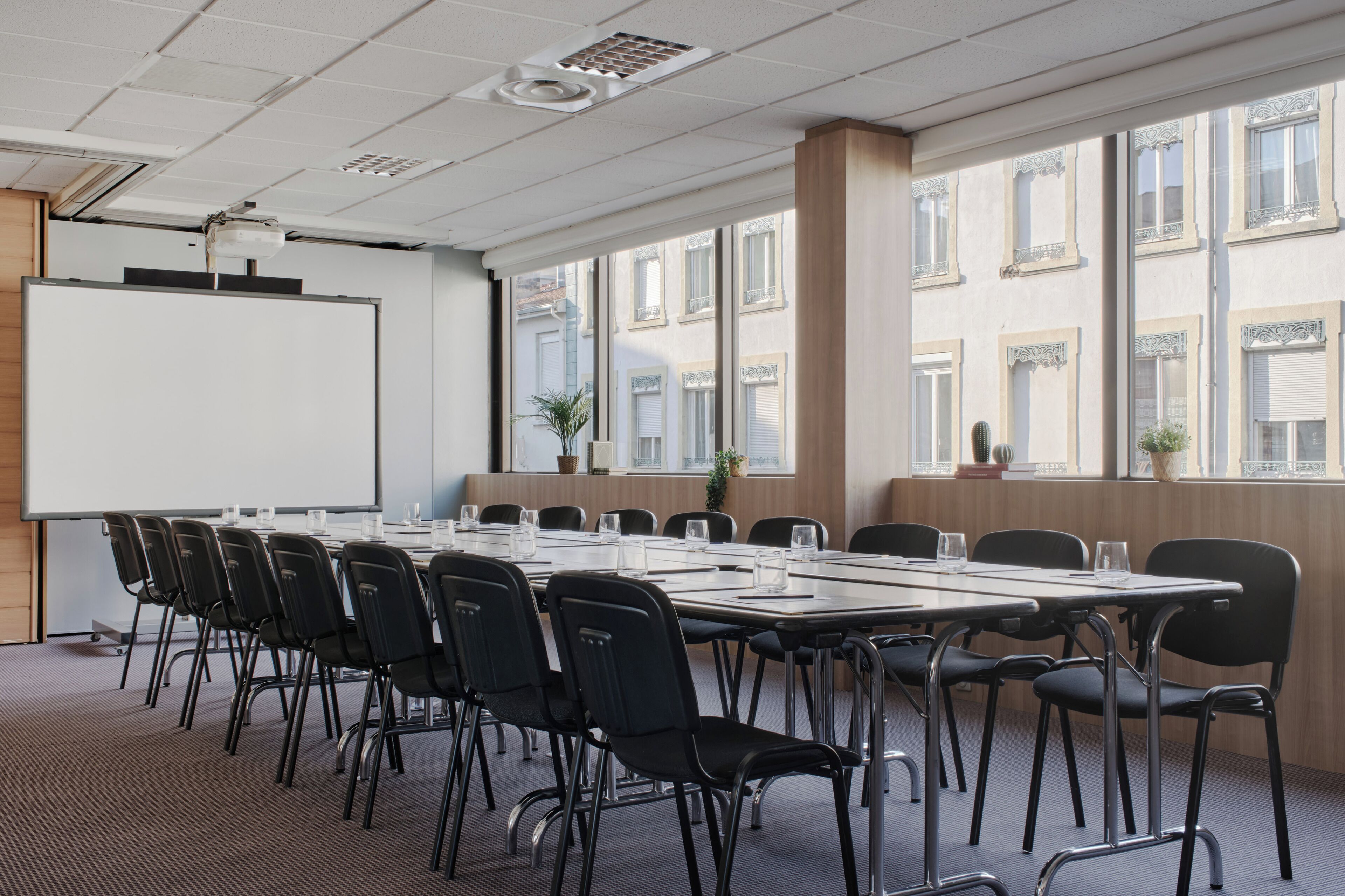 A conference room with a long table, chairs, a whiteboard, and large windows with a view of buildings.
