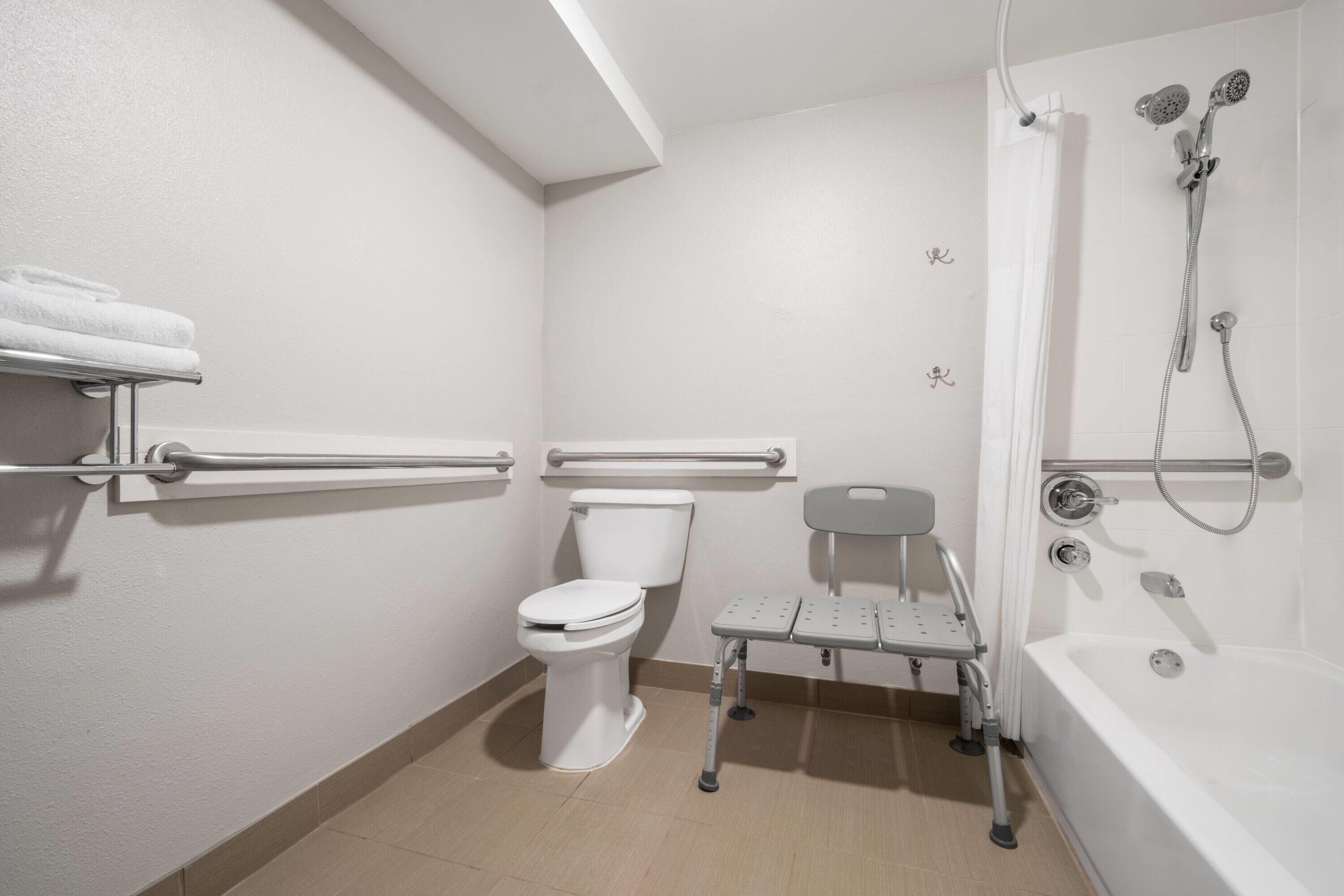 A bathroom with a toilet, grab bars, a shower with a handheld showerhead, and a bathtub.